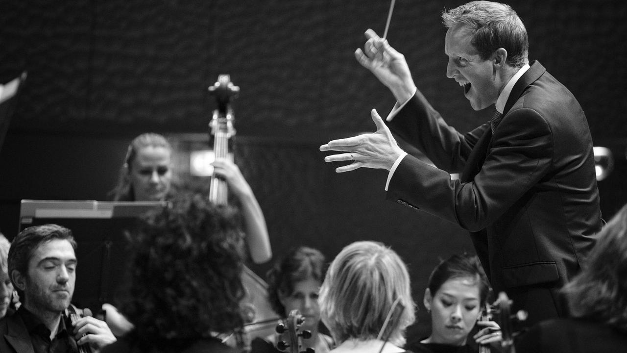 Justin Doyle interagiert vom Pult aus mit den Orchestermusikern. Justin Doyle interagiert vom Pult aus mit den Orchestermusikern.