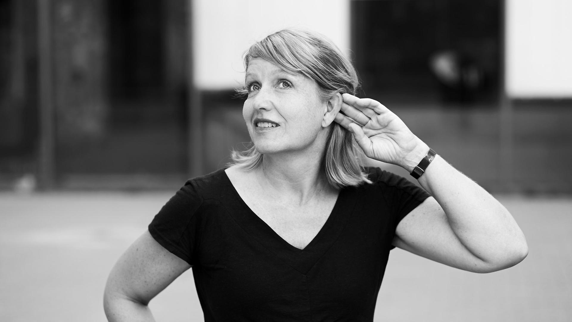 Antje Vowinckel, blonde halblange Haare, schwarzes T-Shirt mit kurzen Ärmeln, hält die linke Hand an ihr Ohr. Antje Vowinckel, blonde halblange Haare, schwarzes T-Shirt mit kurzen Ärmeln, hält die linke Hand an ihr Ohr.