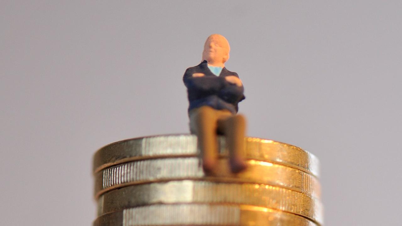 Die Miniatur-Figur eines Rentners, der die Arme verschränkt hat, sitzt auf einem Stapel Euromünzen.