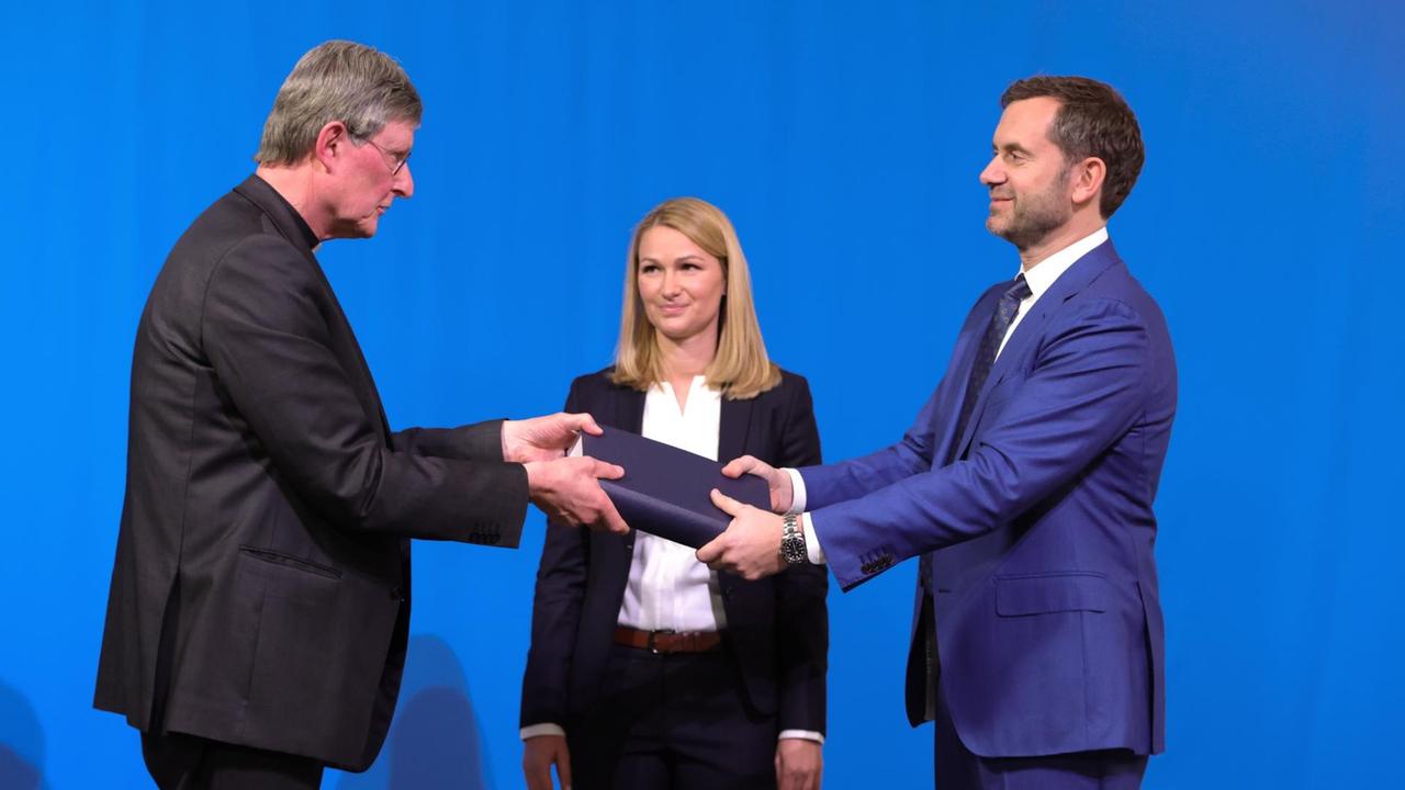 Rechtsanwältin Kerstin Stirner (Mitte) schaut zu, wie der von der Kirche beauftragte Anwalt Björn Gercke (rechts) dem Kölner Erzbischof Rainer Maria Woelki (links) während einer Pressekonferenz ein Exemplar eines Gutachtens zum Umgang des Erzbistums Köln mit sexueller Gewalt übergibt. Rechtsanwältin Kerstin Stirner (Mitte) schaut zu, wie der von der Kirche beauftragte Anwalt Björn Gercke (rechts) dem Kölner Erzbischof Rainer Maria Woelki (links) während einer Pressekonferenz ein Exemplar eines Gutachtens zum Umgang des Erzbistums Köln mit sexueller Gewalt übergibt.