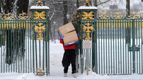 Ein Paketbote, der durch seine Pakete keine freie Sicht hat, trägt in Berlin im Schlosspark Charlottenburg im Schnee unbeirrt seine Lieferung aus.