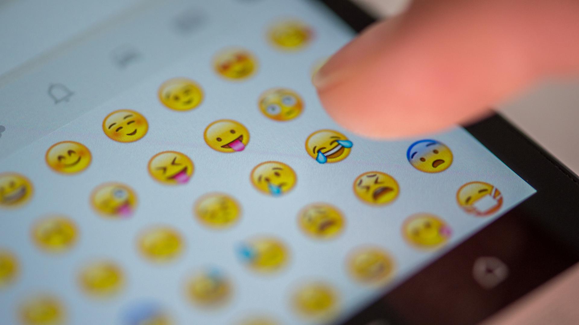 Ein Smartphone-Nutzer tippt auf ein Emoji, um es in eine WhatsApp-Nachricht einzufügen. Ein Smartphone-Nutzer tippt auf ein Emoji, um es in eine WhatsApp-Nachricht einzufügen.