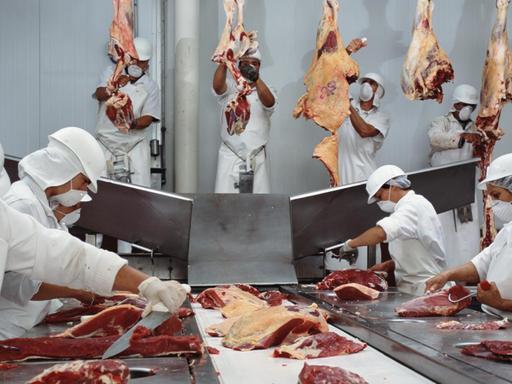 Mitarbeiter eines Schlachtbetriebs zerkleinern Fleisch