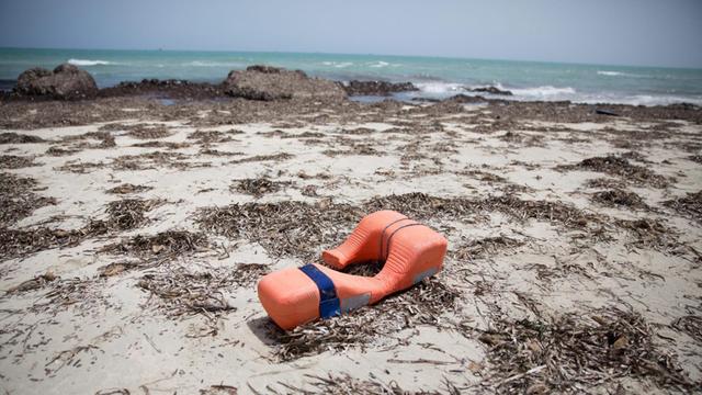 Eine orange Rettungs-Weste liegt auf dem Sand, im Hintergrund das Mittel-Meer. 