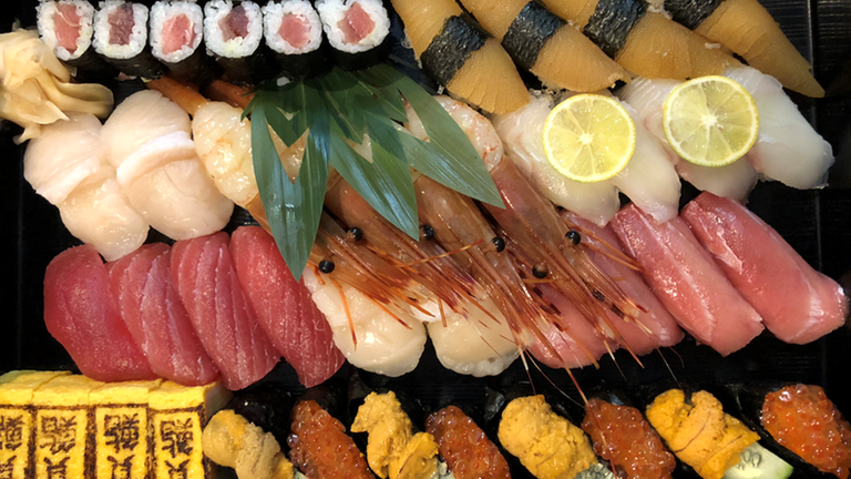 Sushi-Platte mit Nigiri-Röllchen, rohen Jakobsmuscheln, Thunfisch und Seeigel.