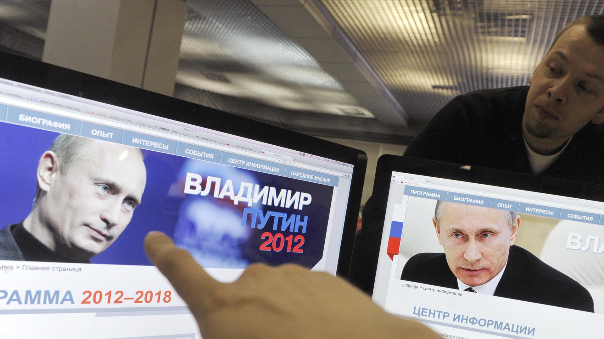 Ein Finger zeigt auf zwei Computerbildschirme, auf denen der russische Präsident Wladimir Putin zu sehen ist. Ein Finger zeigt auf zwei Computerbildschirme, auf denen der russische Präsident Wladimir Putin zu sehen ist.
