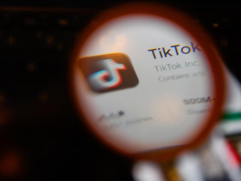 Die App Tik Tok auf einem Smartphonebildschirm durch eine Lupe gesehen.