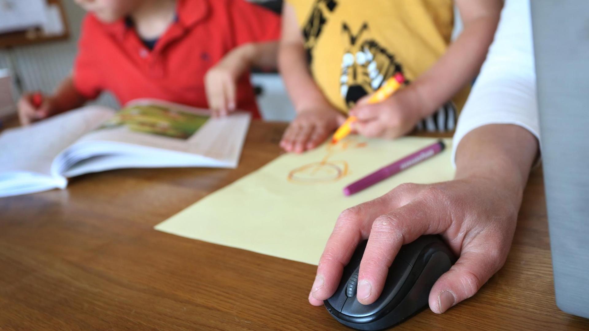 Hand an einer Computermouse; dahinter stehen zwei Kinder Hand an einer Computermouse; dahinter stehen zwei Kinder