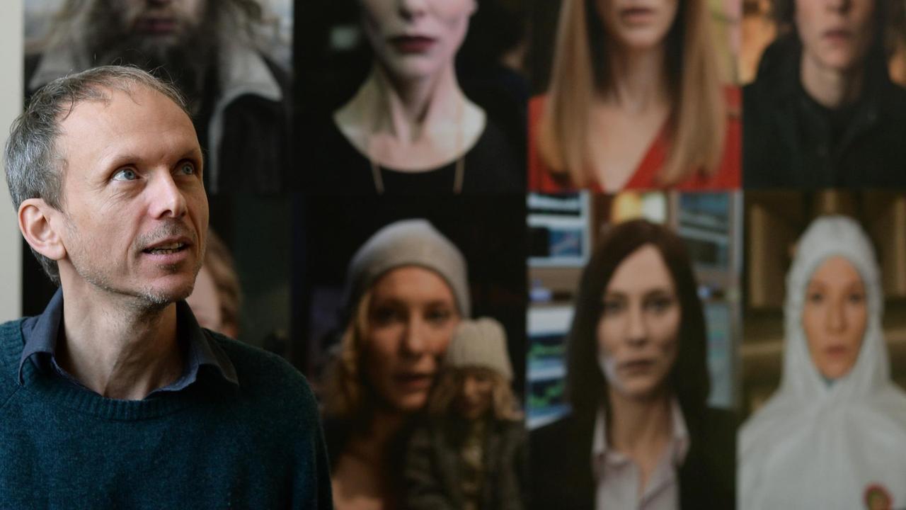 Der Künstler Julian Rosefeldt posiert am 09.02.2016 in Berlin im Hamburger Bahnhof - Museum für Gegenwart in seiner Ausstellung "Manifesto", einer Installation aus 13 parallel laufenden Filmen. Cate Blanchett liest darin die Texte verschiedener Manifeste und spielt in unterschiedlichen Rollen, wie im Hintergrund zu sehen.