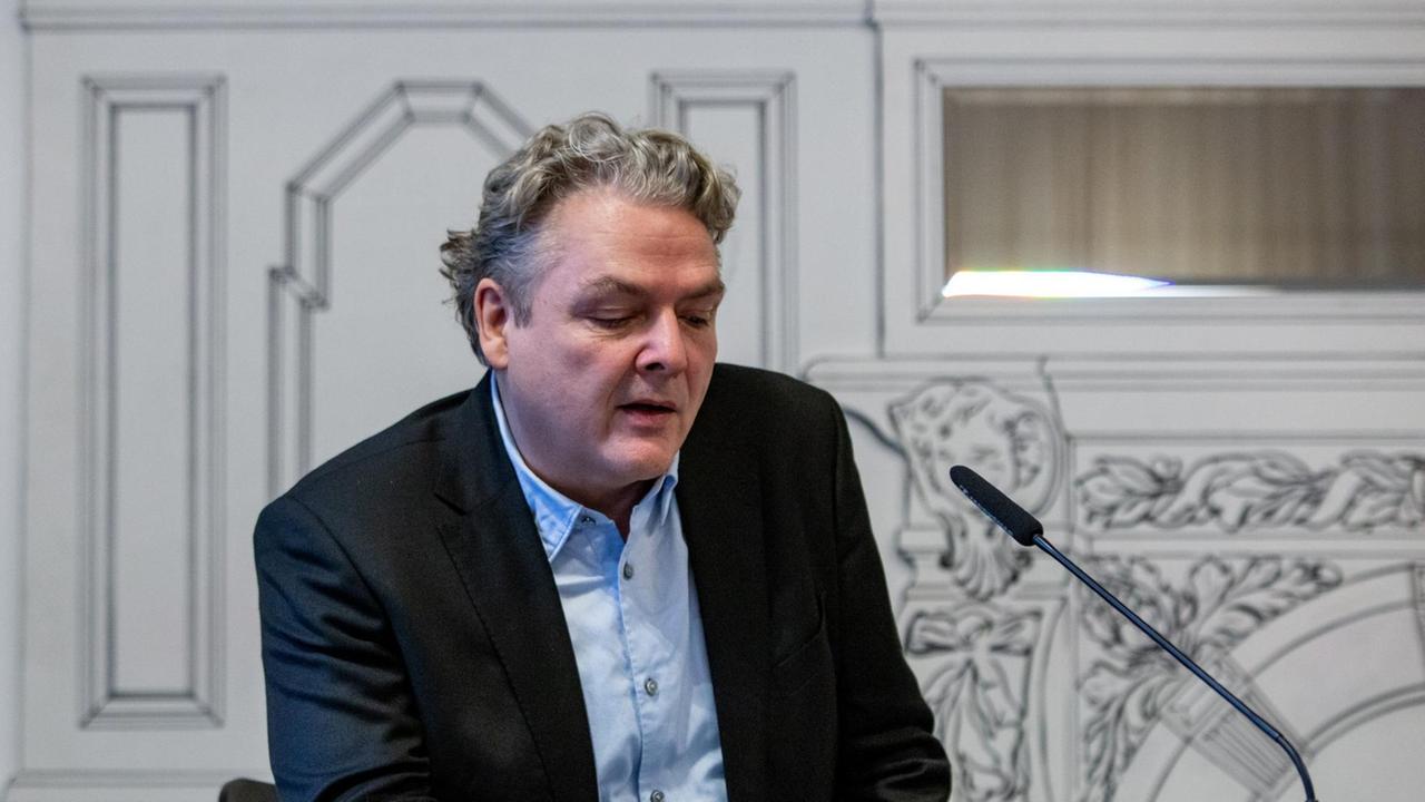 Ein Mann sitzt am Tisch und liest aus einem Buch Ein Mann sitzt am Tisch und liest aus einem Buch