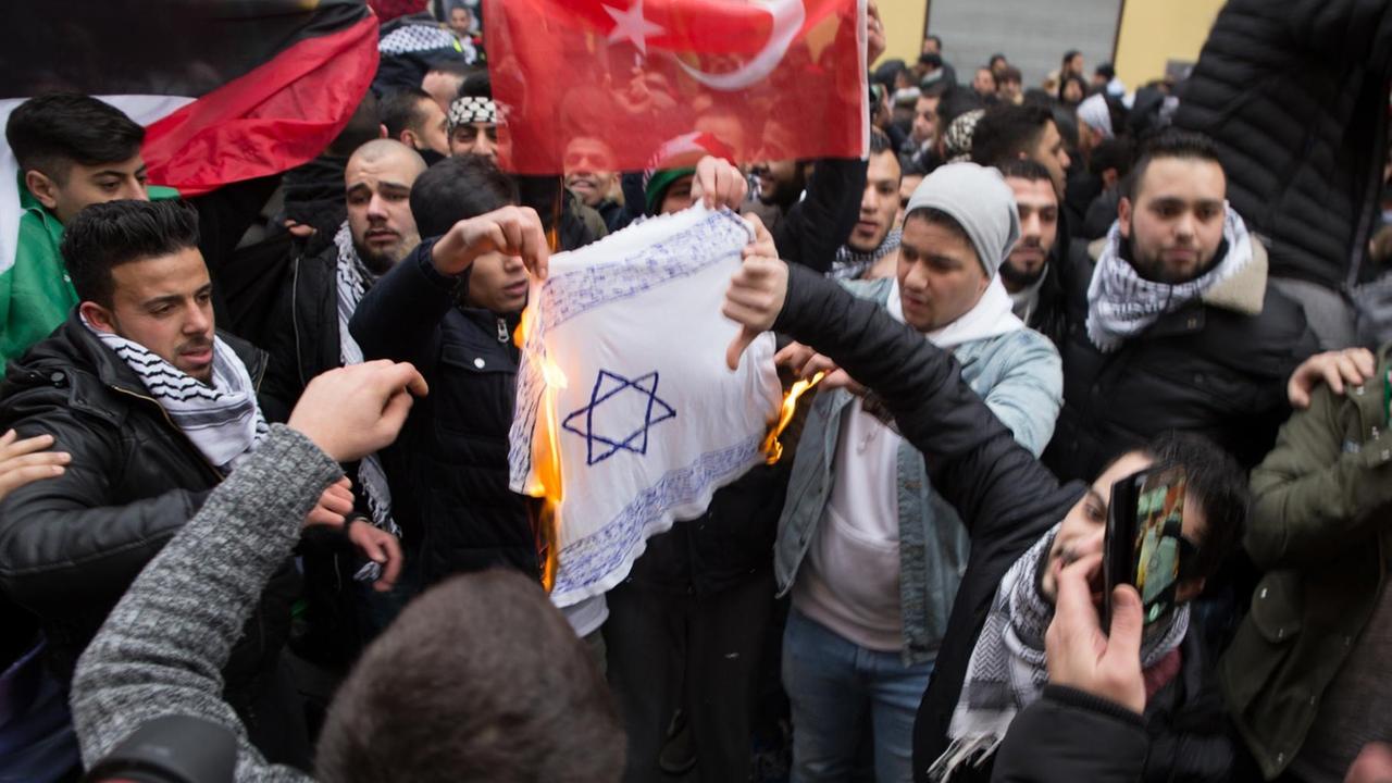 Teilnehmer einer Demonstration verbrennen am 10.12.2017 eine selbstgemalte Fahne mit einem Davidstern in Berlin im Stadtteil Neukölln. Die geplante Verlegung der US-Botschaft in Israel von Tel Aviv nach Jerusalem sorgte auch in Berlin für Proteste. Bei den pro-palästinensischen Demonstrationen wurden Fahnen mit dem Davidstern angezündet. Teilnehmer einer Demonstration verbrennen am 10.12.2017 eine selbstgemalte Fahne mit einem Davidstern in Berlin im Stadtteil Neukölln. Die geplante Verlegung der US-Botschaft in Israel von Tel Aviv nach Jerusalem sorgte auch in Berlin für Proteste. Bei den pro-palästinensischen Demonstrationen wurden Fahnen mit dem Davidstern angezündet.
