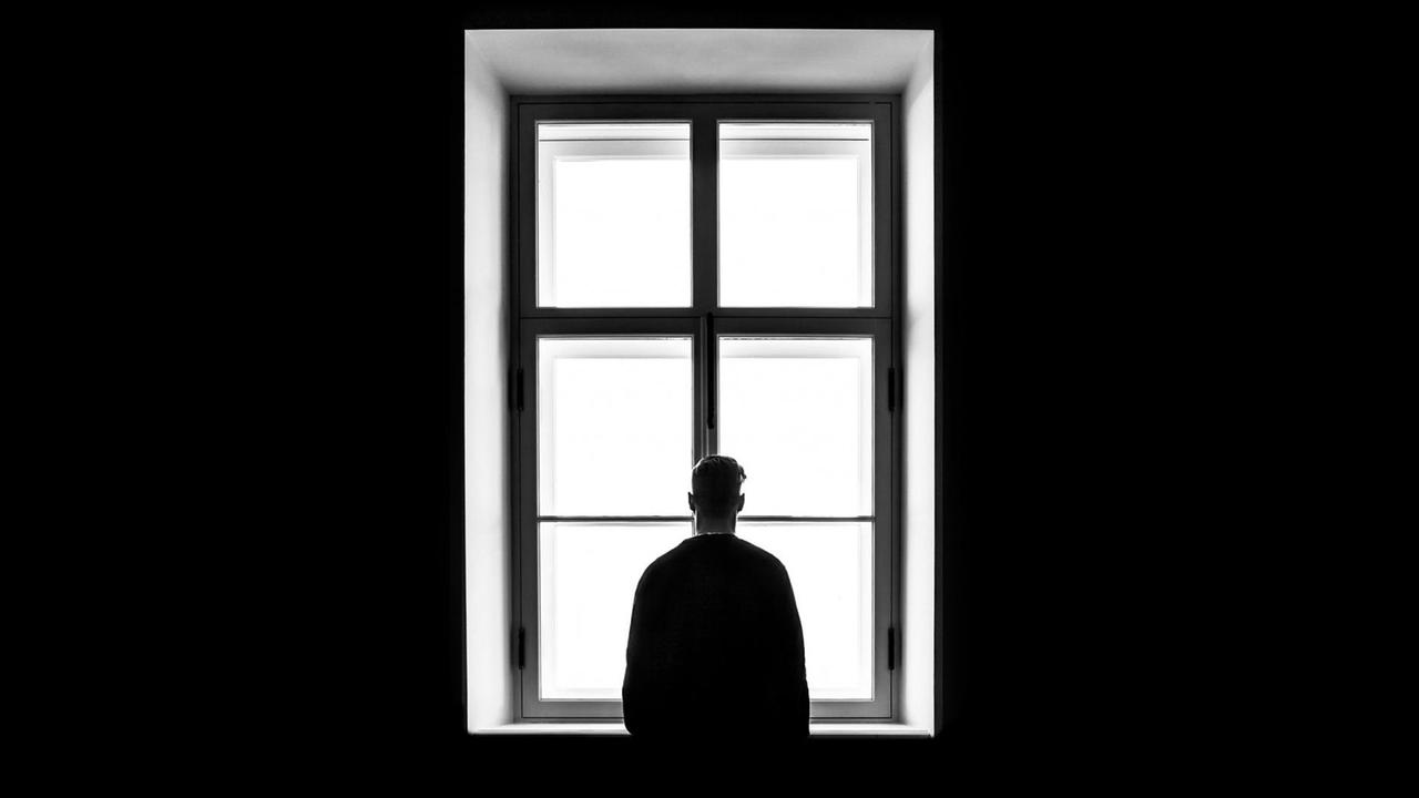 SW-Foto von einem Mann, der dem Betrachter den Rücken zukehrt und vor einem Fenster steht. SW-Foto von einem Mann, der dem Betrachter den Rücken zukehrt und vor einem Fenster steht.
