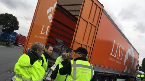 Das Bild zeigt einen orangefarbenen LKW auf einem Autobahnparkplatz zur Abfallkontrolle auf der A2 Im Vordergrund stehen fünf Mitarbeiter der Bezirksregierung Münster.