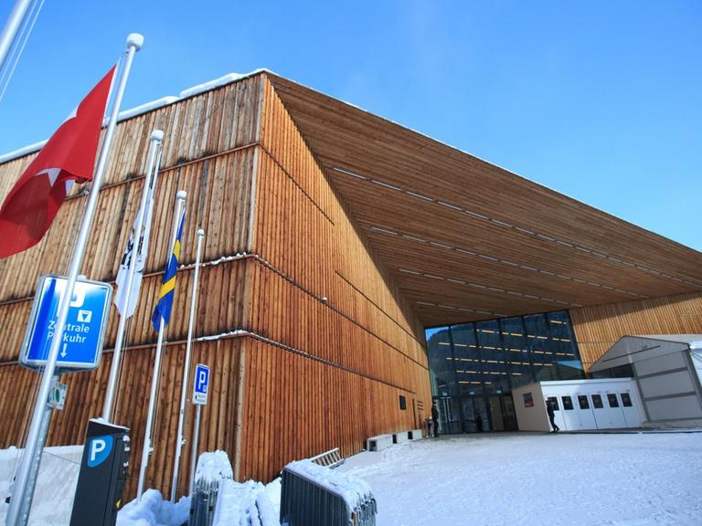 Ein aus einer dramatisierenden Untersicht fotografierter, von Schnee umsäumter, in Brauntönen gehaltener Bau in moderner Architektur.