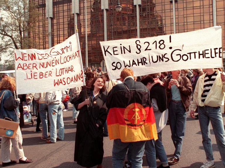Protest am 22. April 1990 gegen eine Übernahme des bundesdeutschen Abtreibungsgesetzes Paragraph 218 vor der Volkskammer in Ost-Berlin. Mehrere Personen halten Transparente hoch.