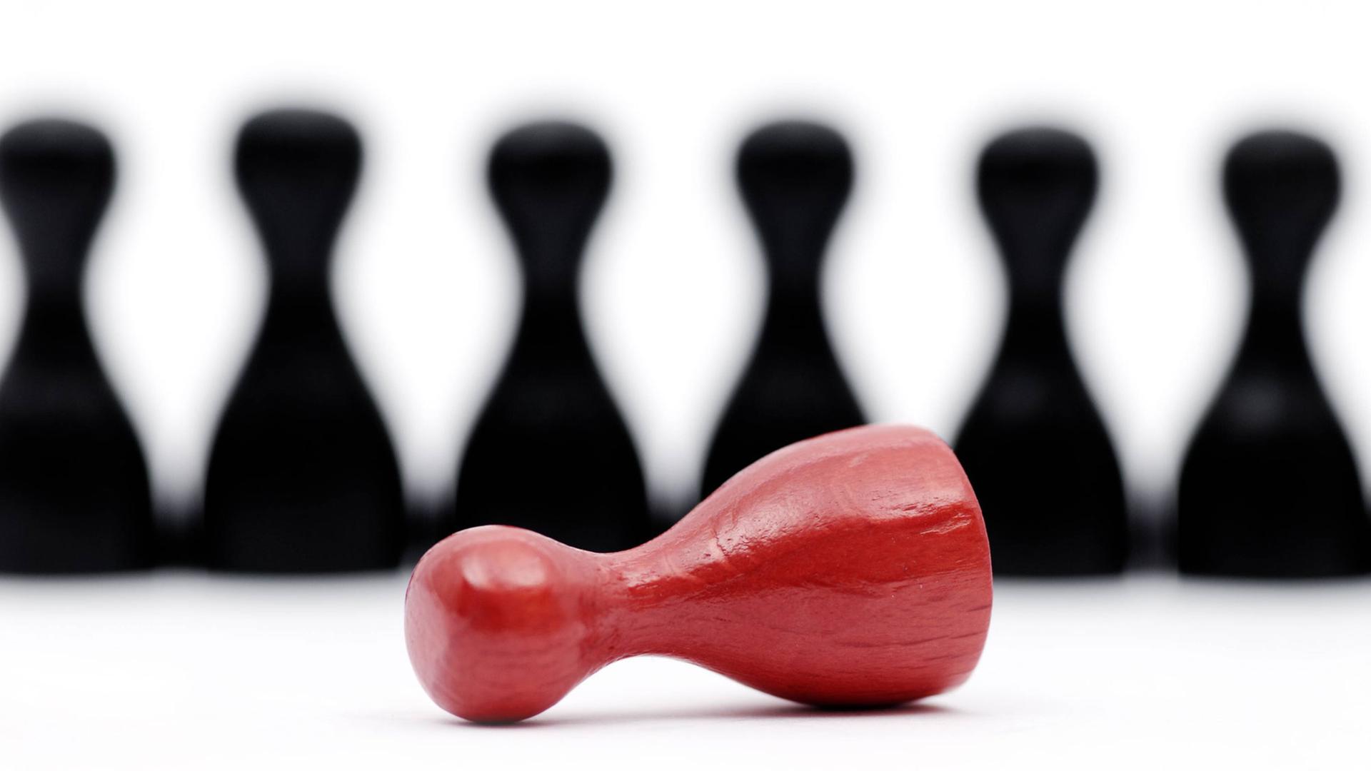 Eine umgefallene rote Spielfigur liegt vor schwarzen Spielfiguren. Eine umgefallene rote Spielfigur liegt vor schwarzen Spielfiguren.