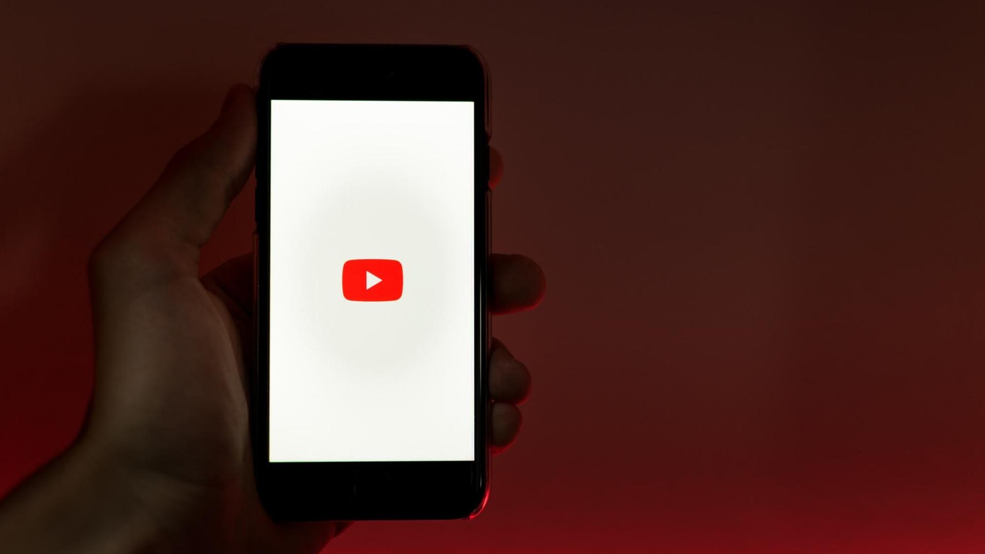 Eine Hand hält ein Smartphone in die Kamera, auf dem das Logo von Youtube abgebildet ist. Eine Hand hält ein Smartphone in die Kamera, auf dem das Logo von Youtube abgebildet ist.