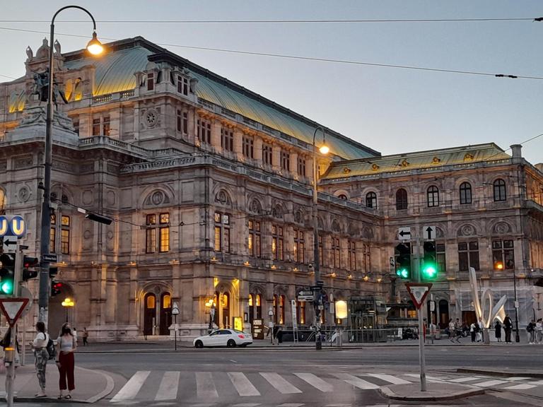 Die Wiender Staatsoper von außen fotografiert. Zu sehen sind ausserdem eine Kreutzung und einige Fußgänger*innen.