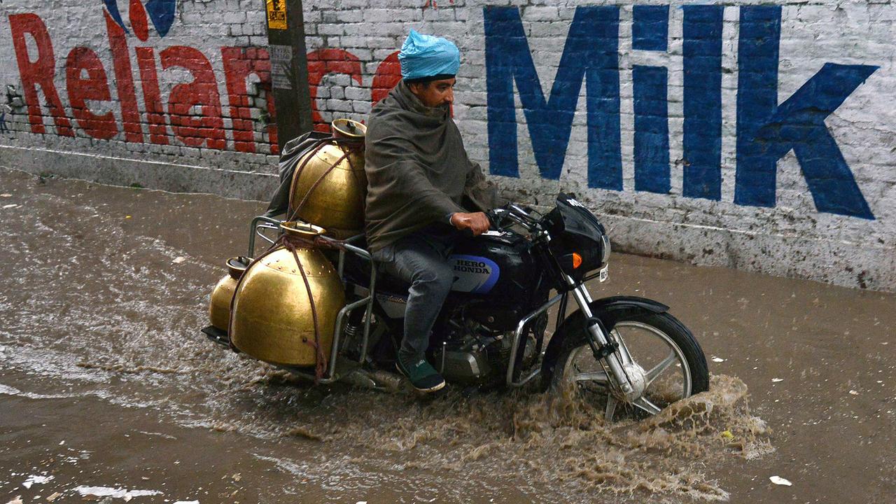 Ein Milchmann im indischen Amritsar fährt auf dem Moped auf einer überfluteten Straße.