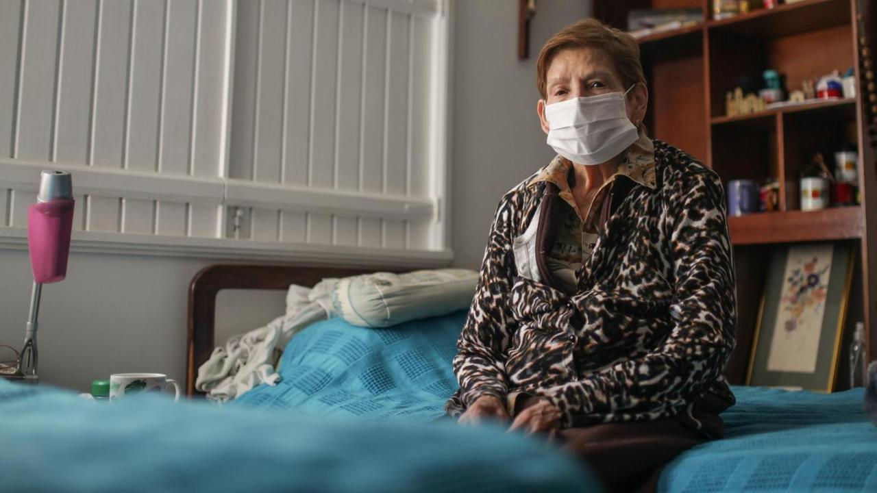 Eine ältere Dame mit Mundschutz sitzt alleine auf einem Bett. Auch in Bogota, Kolumbien werden alle älteren Menschen ab 70 Jahren gebeten, ihr Haus nicht zu verlassen. 18. März 2020 Eine ältere Dame mit Mundschutz sitzt alleine auf einem Bett. Auch in Bogota, Kolumbien werden alle älteren Menschen ab 70 Jahren gebeten, ihr Haus nicht zu verlassen. 18. März 2020
