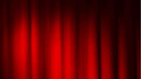 Ein Spot ist auf einen roten Bühnenvorhang gerichtet.
