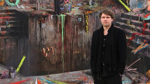 Der Maler Jonas Burgert posiert vor seinem Werk "Luft nach Schlag".