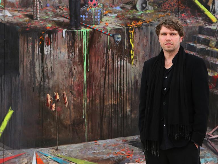 Der Maler Jonas Burgert posiert vor seinem Werk "Luft nach Schlag".