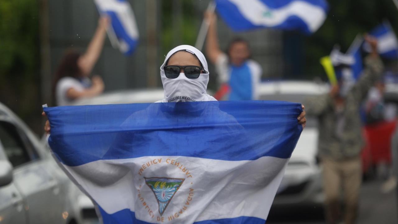 Proteste gegen Präsident Ortega in der Stadt Ticuantepe: Eine Demonstrantin läuft mit nicaraguanischer Nationalfahne zwischen Autos entlang Proteste gegen Präsident Ortega in der Stadt Ticuantepe: Eine Demonstrantin läuft mit nicaraguanischer Nationalfahne zwischen Autos entlang