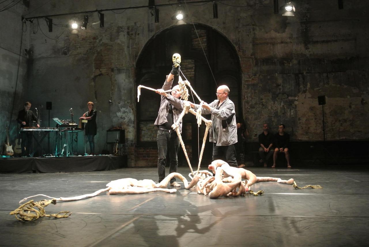 Zwei Puppenspieler hantieren mit schlaksigen Handpuppen. Das Spotlight ist auf sie gerichtet. Zwei Puppenspieler hantieren mit schlaksigen Handpuppen. Das Spotlight ist auf sie gerichtet.