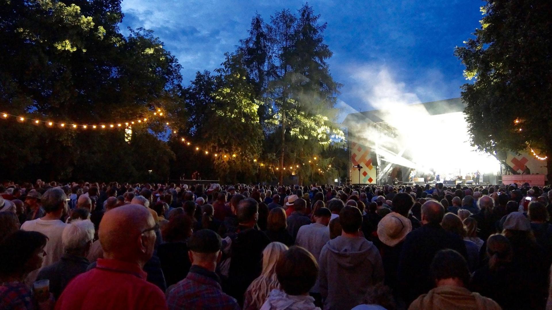 Eine Menschenmenge steht auf dem Rasen vor einer Bühne im Hintergrund während des Rudolstadtfestival Eine Menschenmenge steht auf dem Rasen vor einer Bühne im Hintergrund während des Rudolstadtfestival