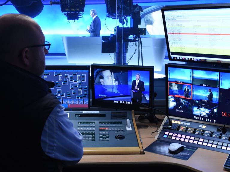 Ein Redakteur sitzt im Regieraum der ARD-Tagesschau vor eine Reihe Fernseh- und Computermonitoren.