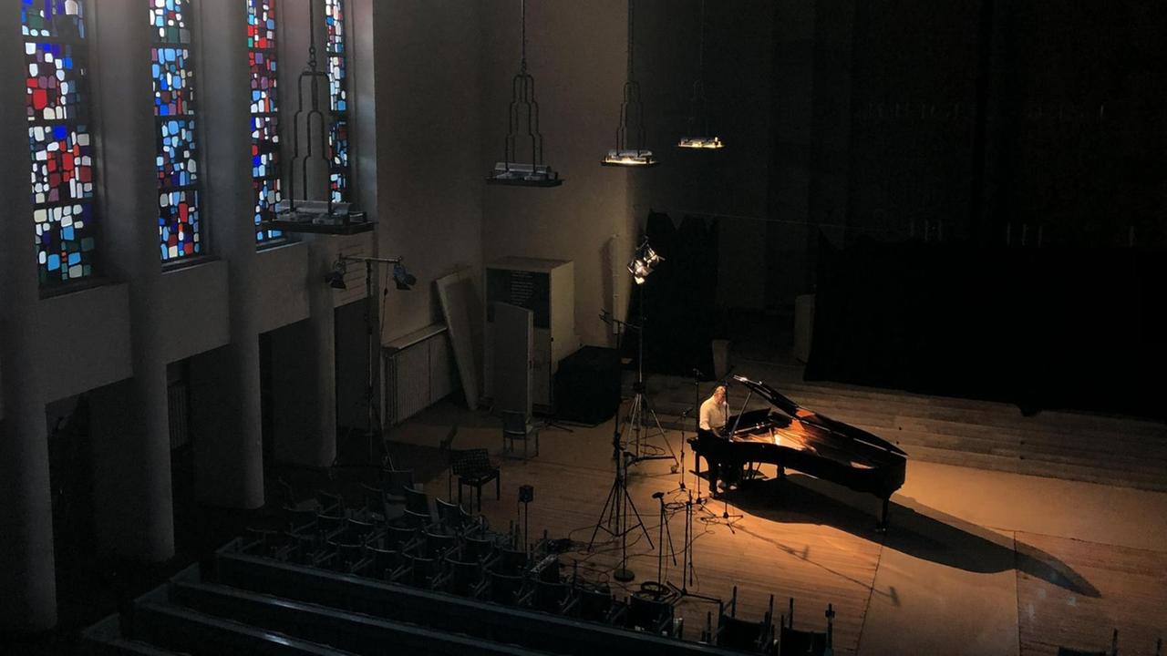 In einer leeren Kirche wird buntes Licht auf einen Flügel mit Pianisten geworfen.