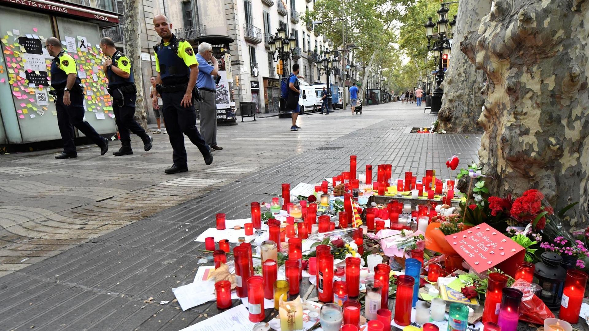 Polizisten patrouillieren entlang des Boulevards Las Ramblas in Barcelona. Auf der Straße stehen Kerzen, die an die Opfer des Terroranschlags erinnern.