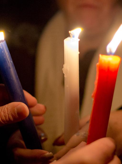 Teilnehmer eines stillen Gedenkens für die Opfer der Terroranschläge in Paris halten in Nürnberg Kerzen in den Farben der französischen Flagge - blau-weiß-rot - in den Händen.
