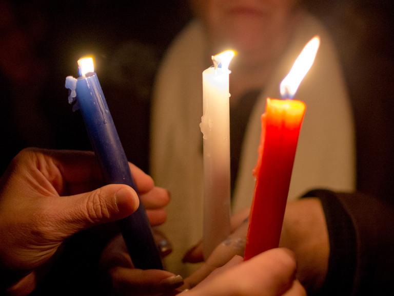Teilnehmer eines stillen Gedenkens für die Opfer der Terroranschläge in Paris halten in Nürnberg Kerzen in den Farben der französischen Flagge - blau-weiß-rot - in den Händen.