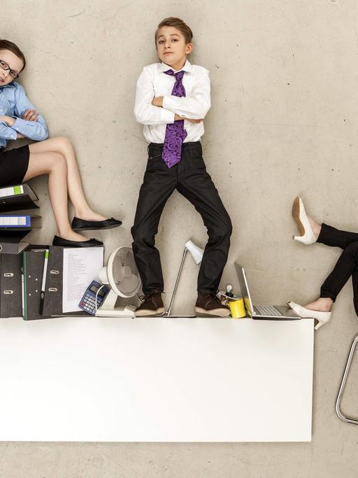 Drei selbstbewusste Teenager im Business-Look stehen und sitzen auf Aktenordnern und Büromöbeln