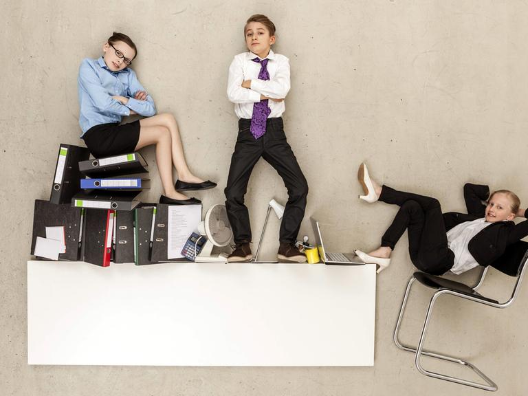 Drei selbstbewusste Teenager im Business-Look stehen und sitzen auf Aktenordnern und Büromöbeln