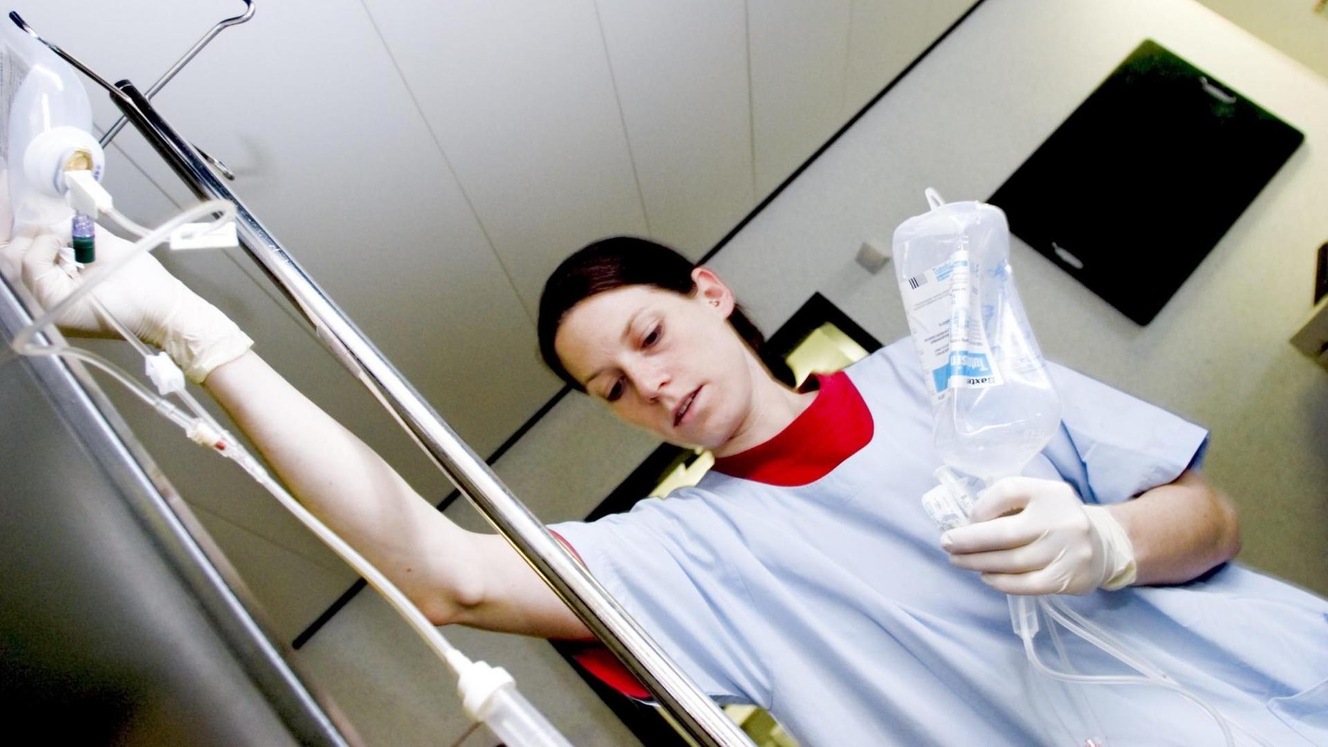 Eine Krankenschwester kontrolliert die Infusion am Krankenbett einer Patientin. München, Bayern.