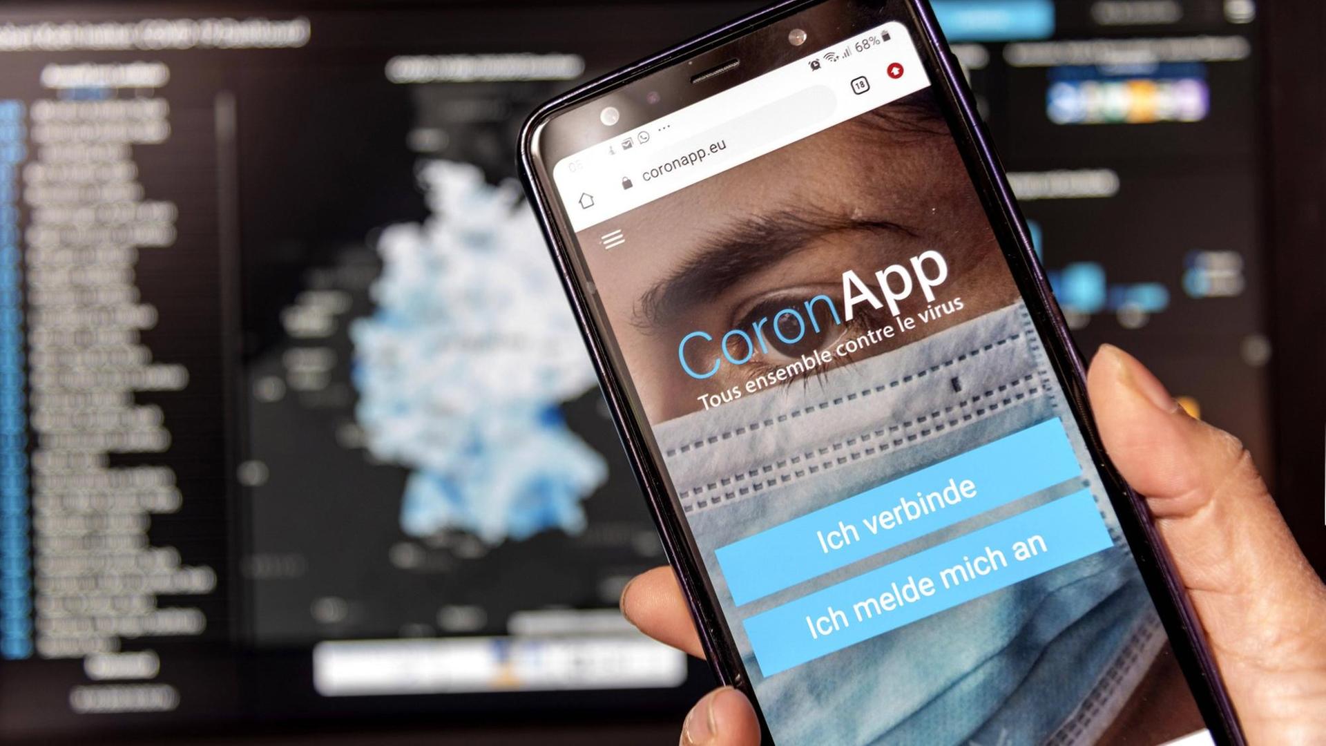 Die Freiwilige Corona-App app.coronapp.eu läuft auf einem Smartphone, im Hintergrund ist die Website des Robert Koch Instituts zu sehen.
