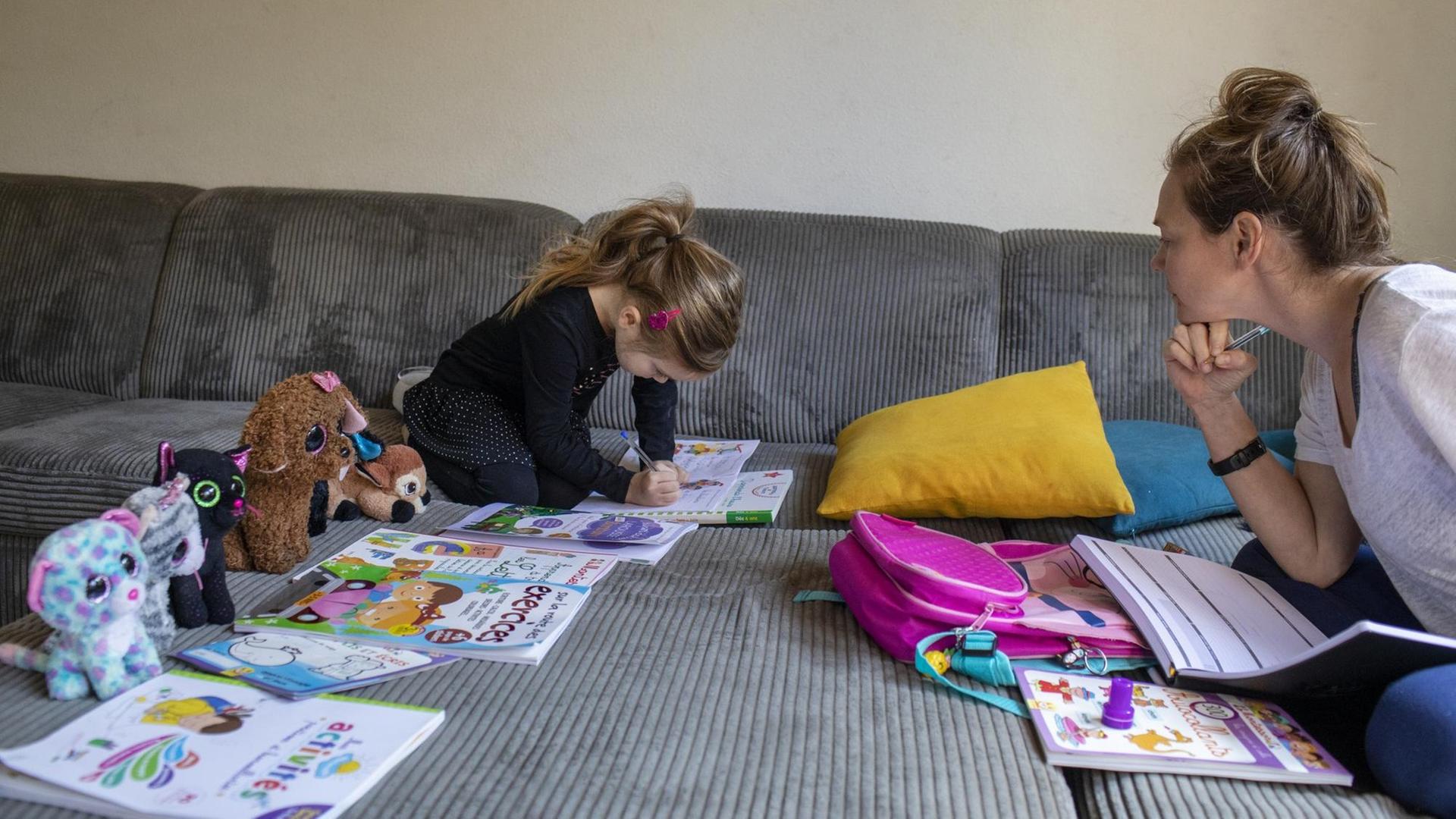 Abby, 6, mit ihrer Mutter Lisa beim Homeschooling auf dem Sofa zu Hause. Die Kuscheltiere sitzen auch alle vor einem Arbeitsheft. 20. März 2020 in Claira, Frankreich. Abby, 6, mit ihrer Mutter Lisa beim Homeschooling auf dem Sofa zu Hause. Die Kuscheltiere sitzen auch alle vor einem Arbeitsheft. 20. März 2020 in Claira, Frankreich.
