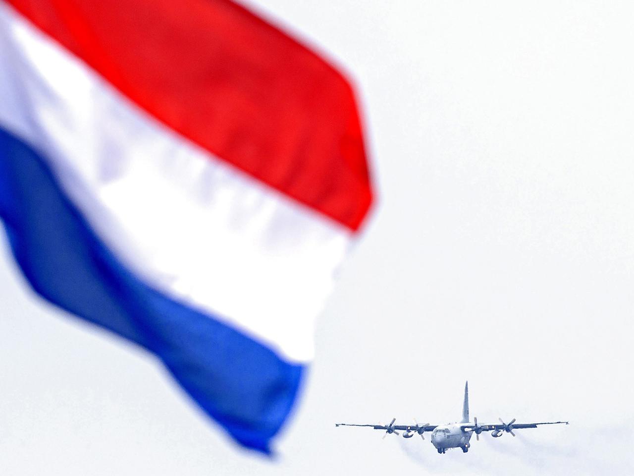 Transportmaschine des Militärs im Landeanflug, im Vordergrund weht die niederländische Flagge.