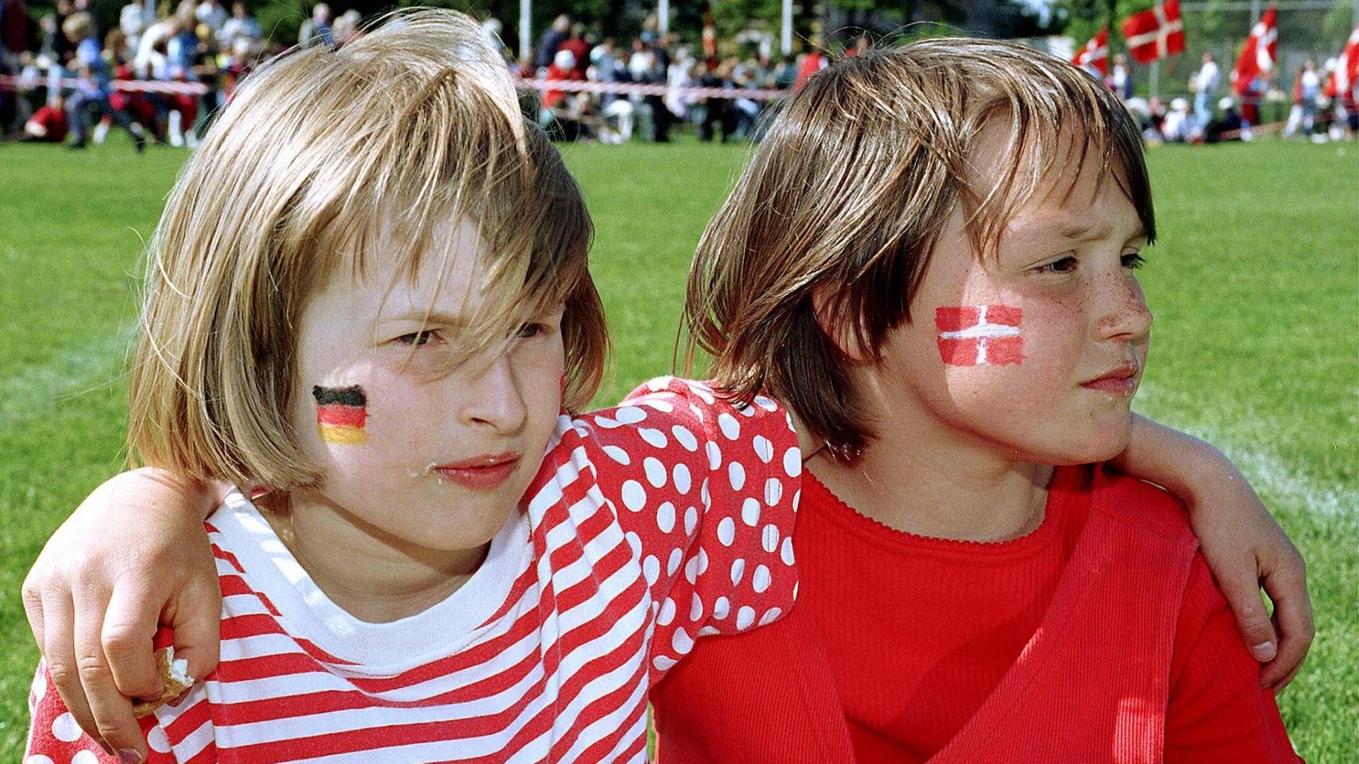 Zwei Kinder Arm in Arm auf einem Volksfest der dänischen Minderheit in Südschleswig, eins mit einer dänischen Flagge, eins mit einer deutschen auf die Wange geschminkt Zwei Kinder Arm in Arm auf einem Volksfest der dänischen Minderheit in Südschleswig, eins mit einer dänischen Flagge, eins mit einer deutschen auf die Wange geschminkt