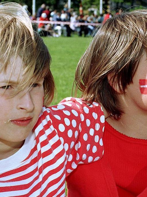Zwei Kinder Arm in Arm auf einem Volksfest der dänischen Minderheit in Südschleswig, eins mit einer dänischen Flagge, eins mit einer deutschen auf die Wange geschminkt