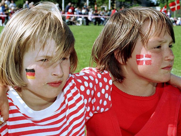 Zwei Kinder Arm in Arm auf einem Volksfest der dänischen Minderheit in Südschleswig, eins mit einer dänischen Flagge, eins mit einer deutschen auf die Wange geschminkt