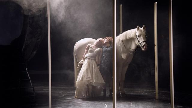 Eine Szene aus "Melancholia" nach dem Film von Lars von Trier am Schauspielhaus Bochum: Ein weisses Pferd und zwei Schauspielerinnen stehen zwischen Stelen auf der Bühne.