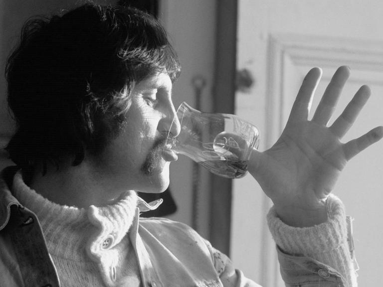 Der Designer Luigi Colani trinkt aus einem Weinglas, das statt eines Stiels eine Vertiefung für den Daumen im Boden hat.