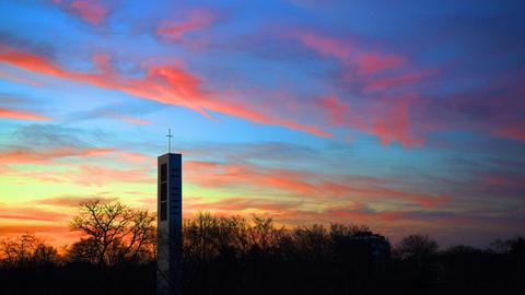 Die letzten Strahlen der untergehenden Sonne faerben die Wolken, die hinter dem Turm der Evangelischen Thomaskirche am Himmel stehen, rosa.