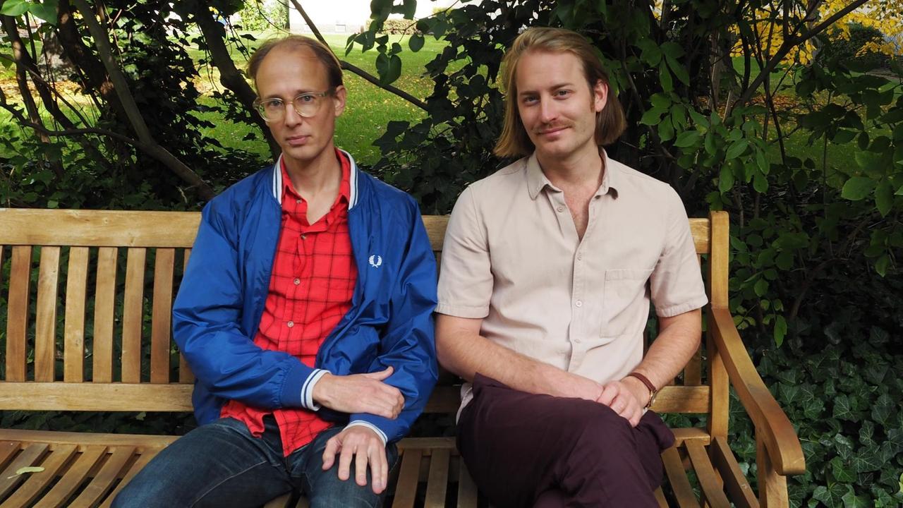 Andreas Engström und Bastian Zimmermann vom Editorial Team der Zeitschrift positionen, sitzen nebeneinander auf einer Gartenbank.