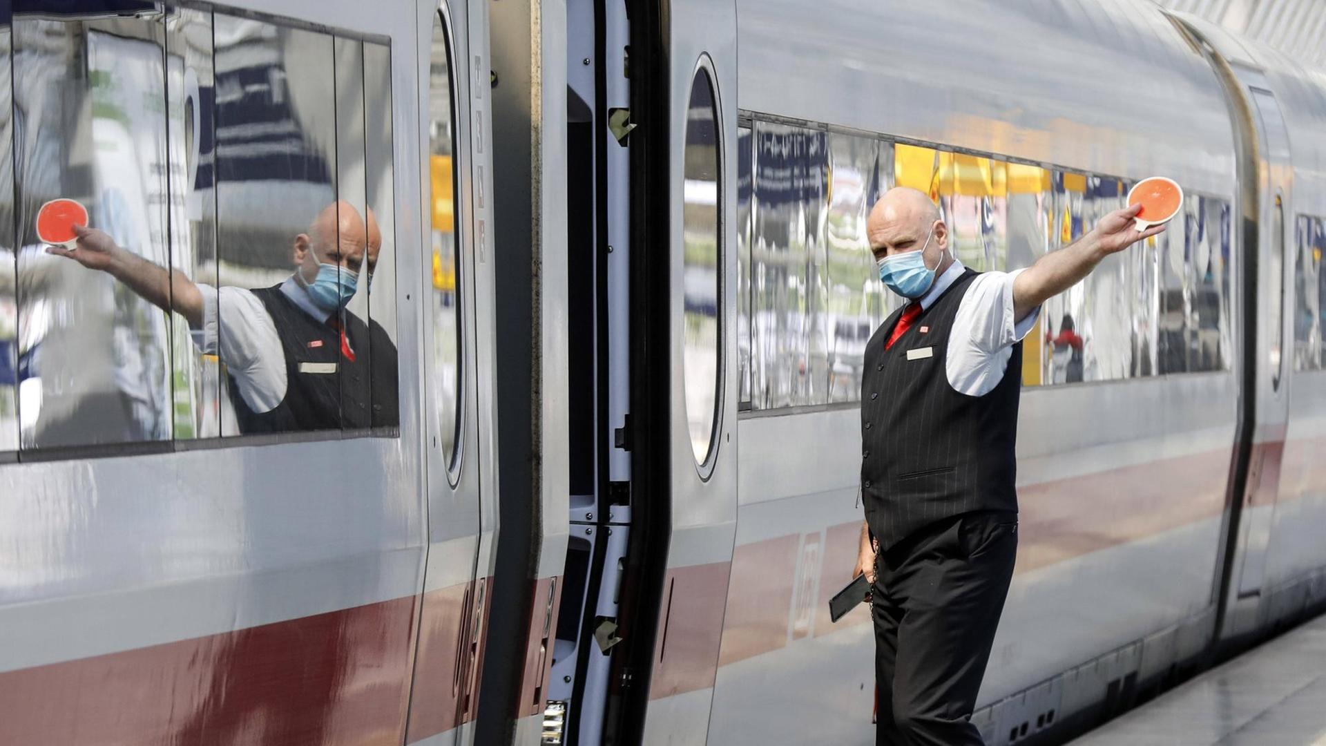 Ein Zugbegleiter mit Gesichtsmaske gibt dem Lokfuehrer das Abfahrtzeichen im Bahnhof Berlin Spandau.