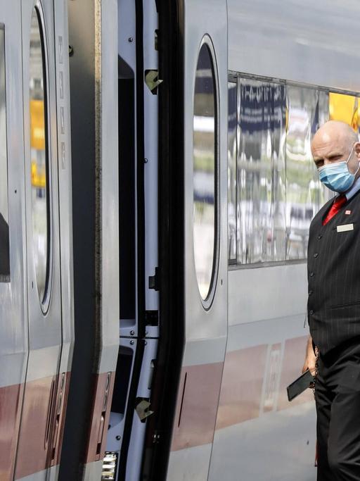 Ein Zugbegleiter mit Gesichtsmaske gibt dem Lokfuehrer das Abfahrtzeichen im Bahnhof Berlin Spandau.